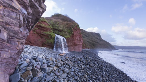 Waterfall in spilling onto a grey pebble beach with the sea and cliffs surrounding